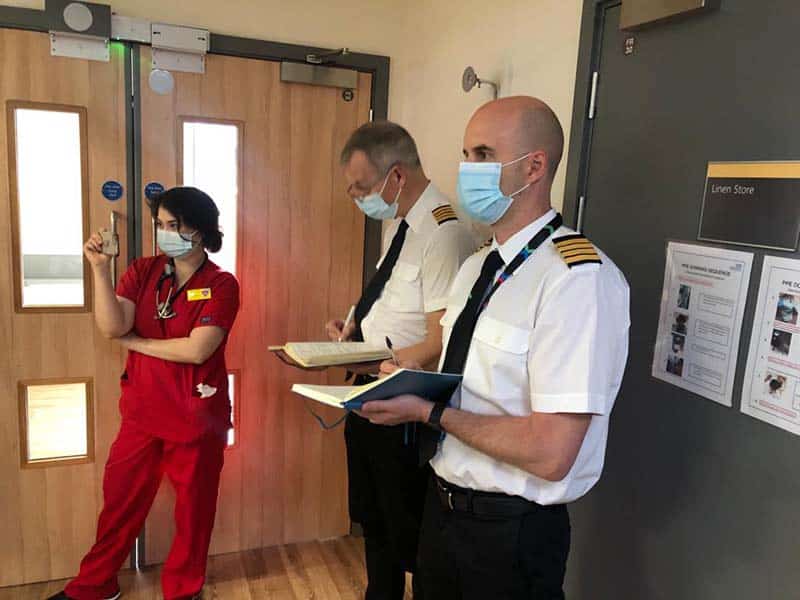 Two airline pilots observing an NHS clinical simulation and taking notes for human factors feedback